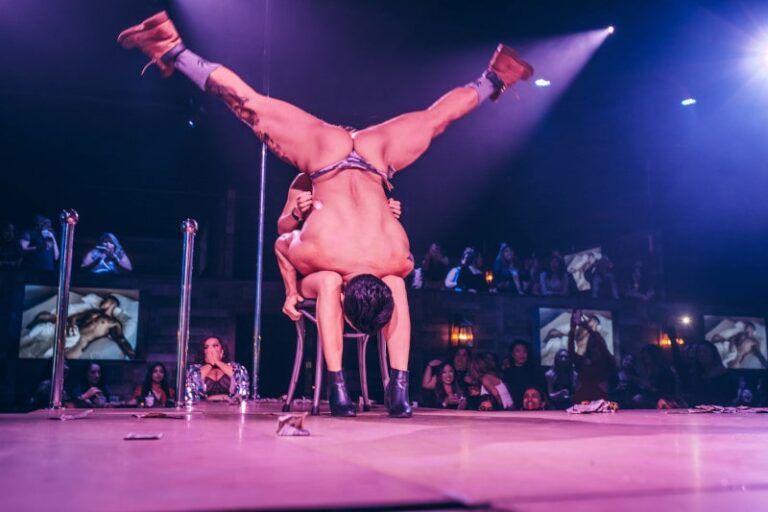 male stripper wearing thong gets vertical with lady seated in chair on stage