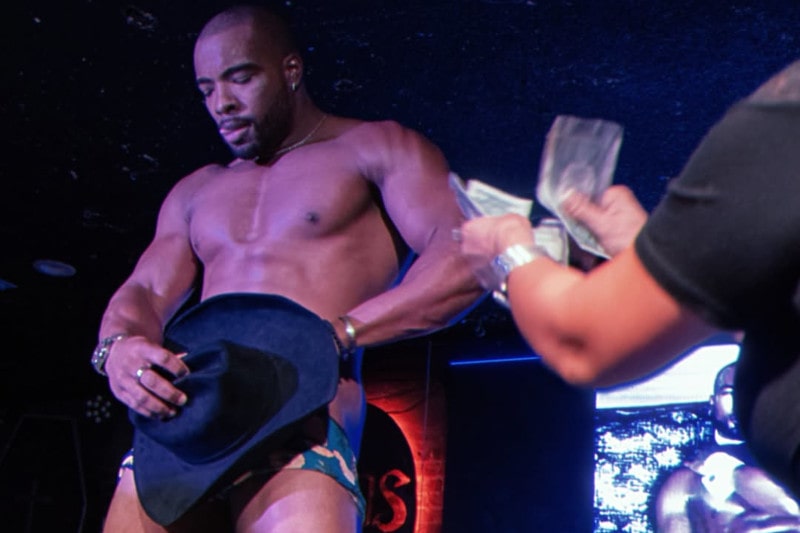 black male cowboy stripper on stage covering pelvis with cowboy hat