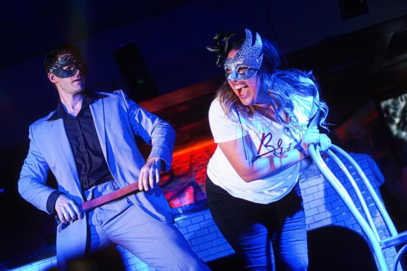 fifty shades of grey strip act showing christian grey about to spank lady bent over chair on stage